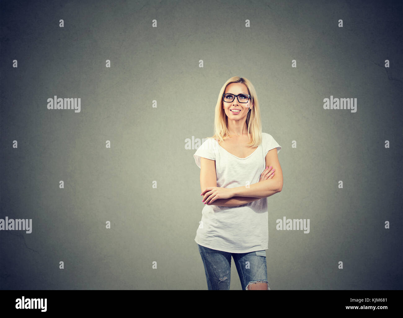 Portrait of happy woman thinking looking up while standing near a concrete wall. Stock Photo