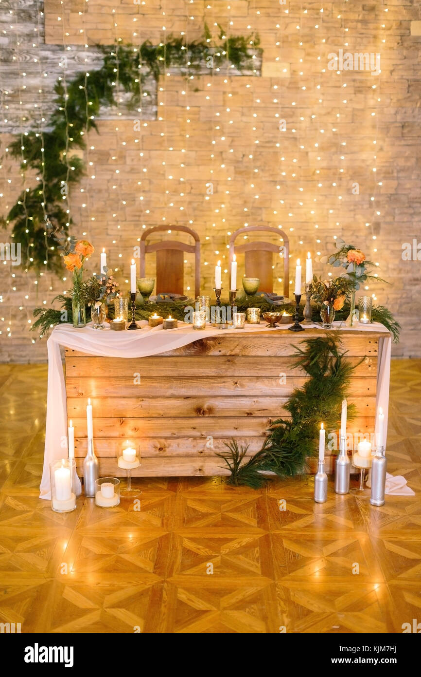 catering, dining, wedding concept. in the shining dining hall with walls decorated by twinkle lights there are table for bride and groom, surrounded by burning candles Stock Photo