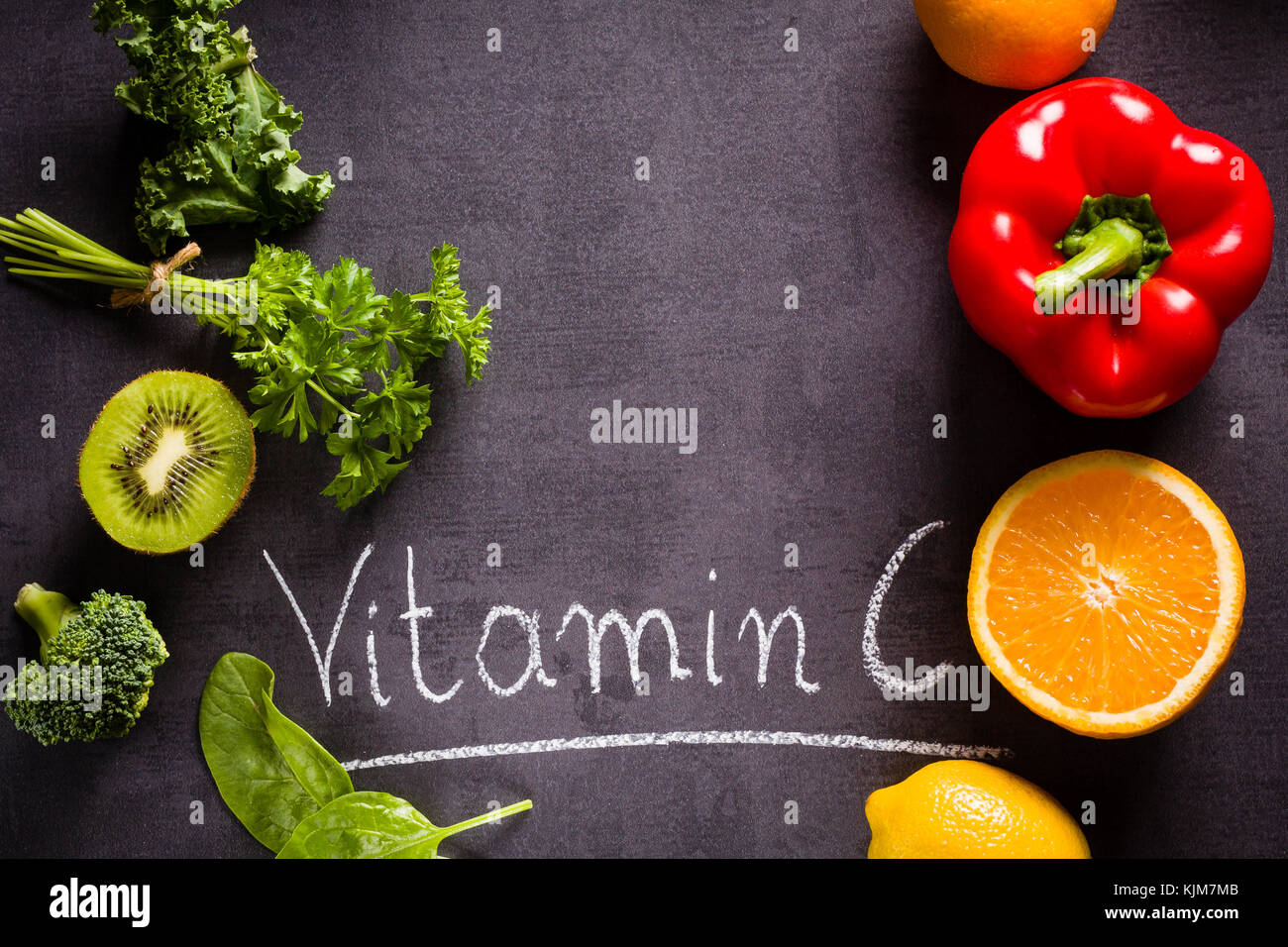 Fruits and vegetables rich in vitamin C with white word inscription by chalk and copy space on black slate. Stock Photo