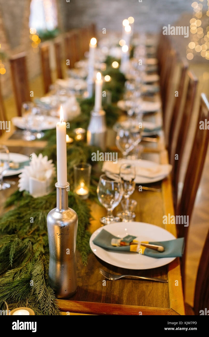 wedding decor, interior, illumination concept. close up of served holiday table with candles in original holders that looks like bottles, among them there are fresh branches of conifer trees Stock Photo
