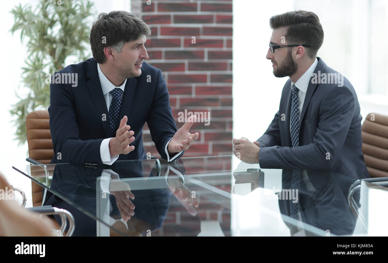 Two businessmen discussing tasks sitting at office table Stock Photo ...