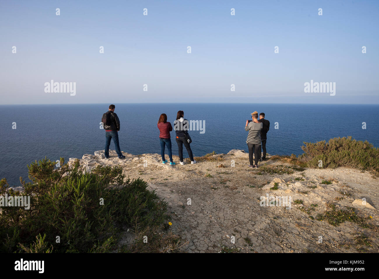 Group of people on the top of the cliff, overlooking at sea. Stock Photo