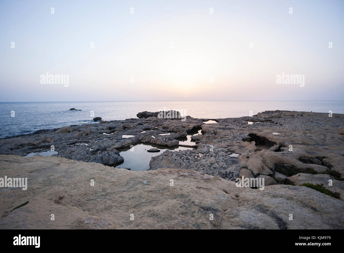 Sunset hour at Dwejra Bay, looking at sea, with rocky shore foreground. Stock Photo