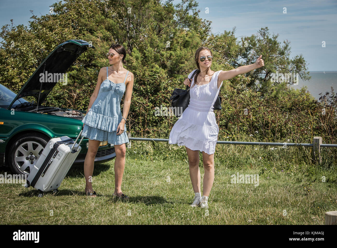 Two beautiful young women on a summer road trip with their broken down convertible car. Stock Photo