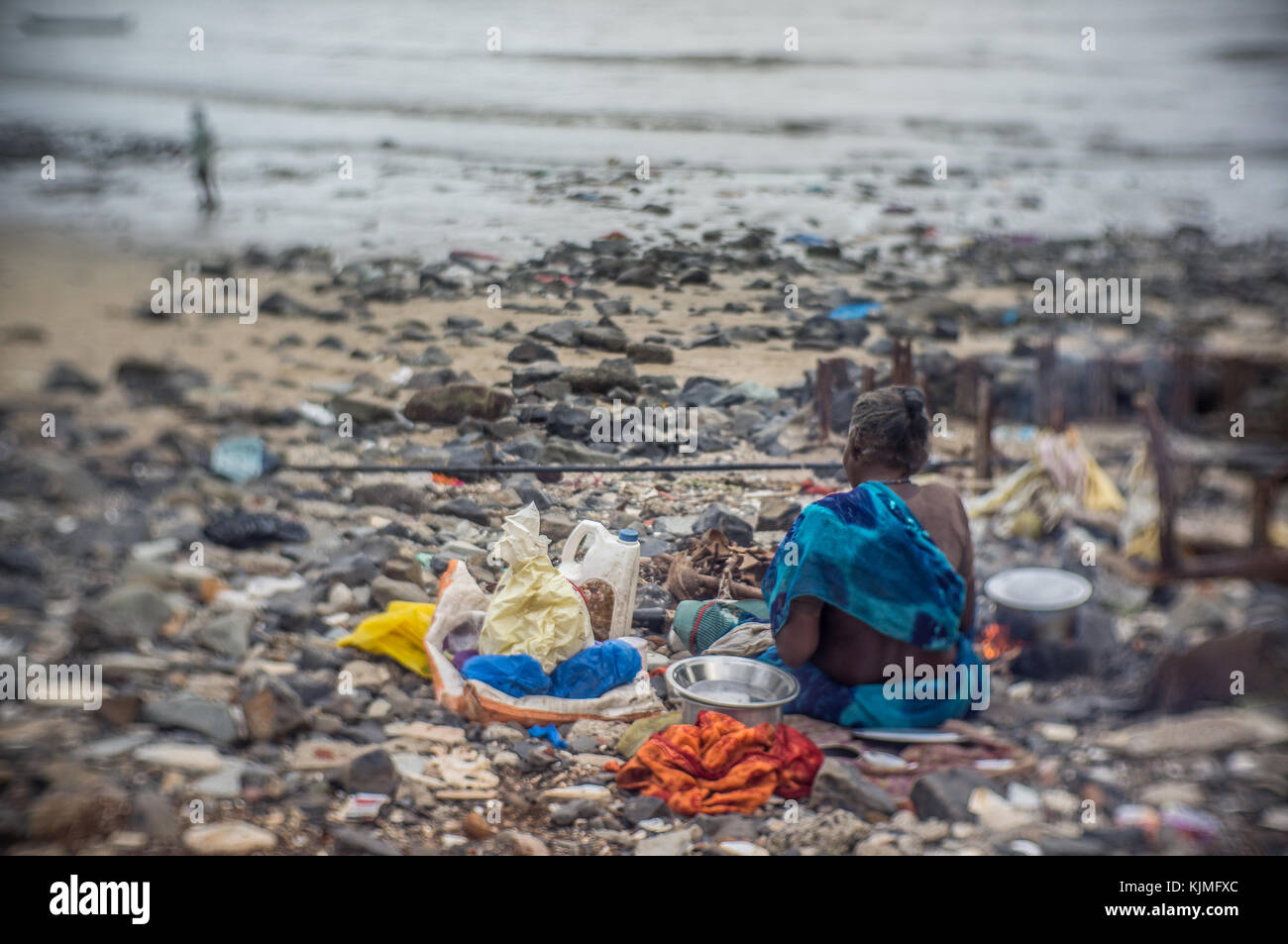 A homeless woman sitting in her camp by the water in India. Stock Photo