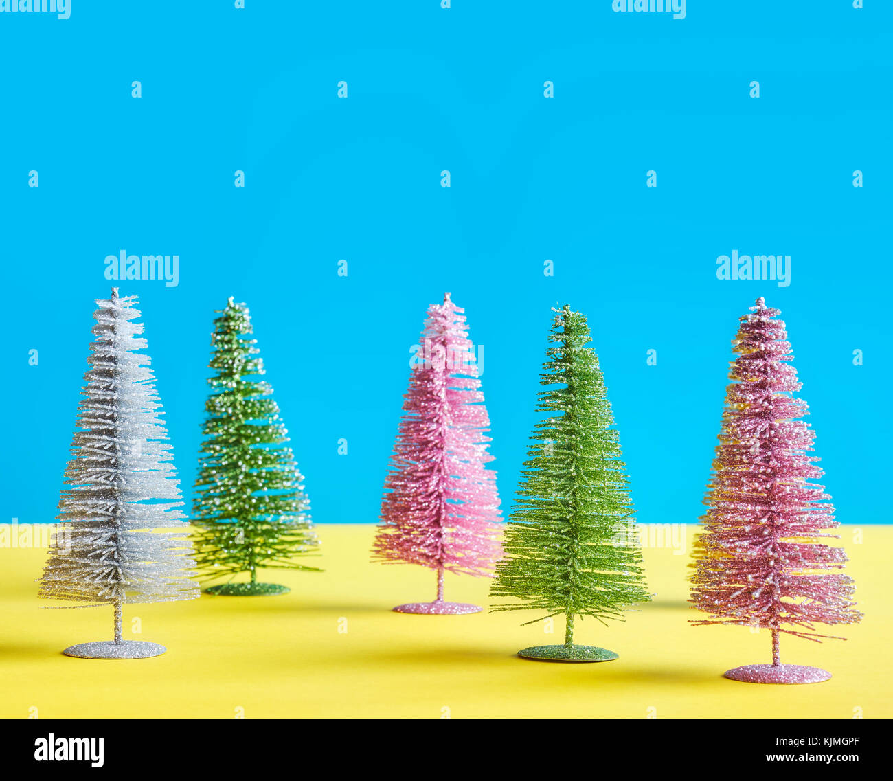 Miniature multicolored Christmas trees on blue and yellow background, space for text. Stock Photo
