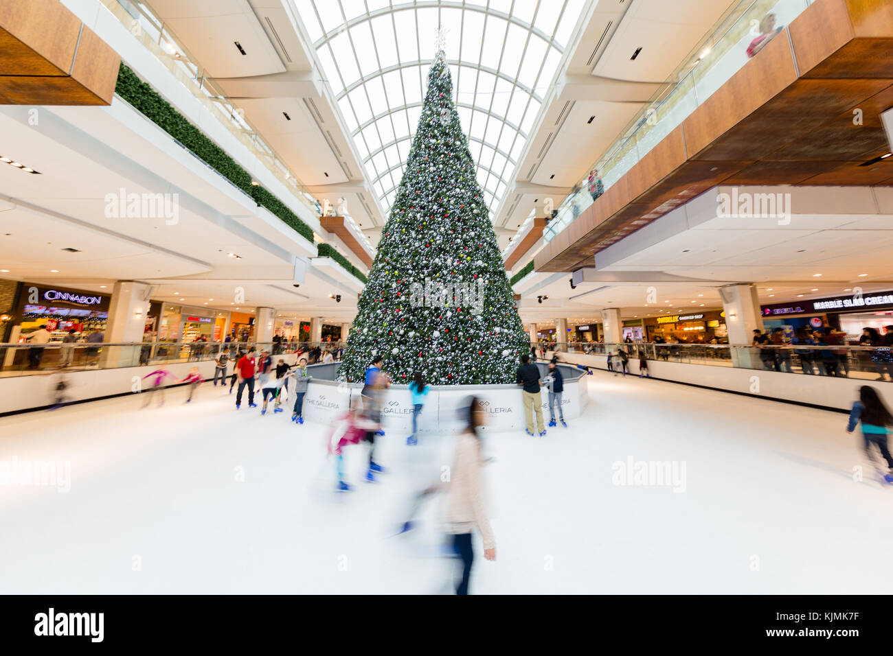 Children and Young Adults Ice Skating Around Christmas Tree in Skate Rink in a Large Indoor Shopping Mall Stock Photo