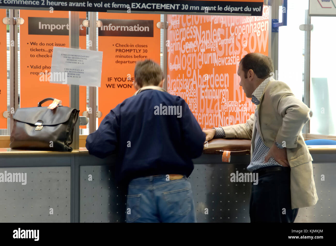 2 businessmen passengers with carry-on baggage at the easyJet ticket sales booth in Terminal3 Stock Photo