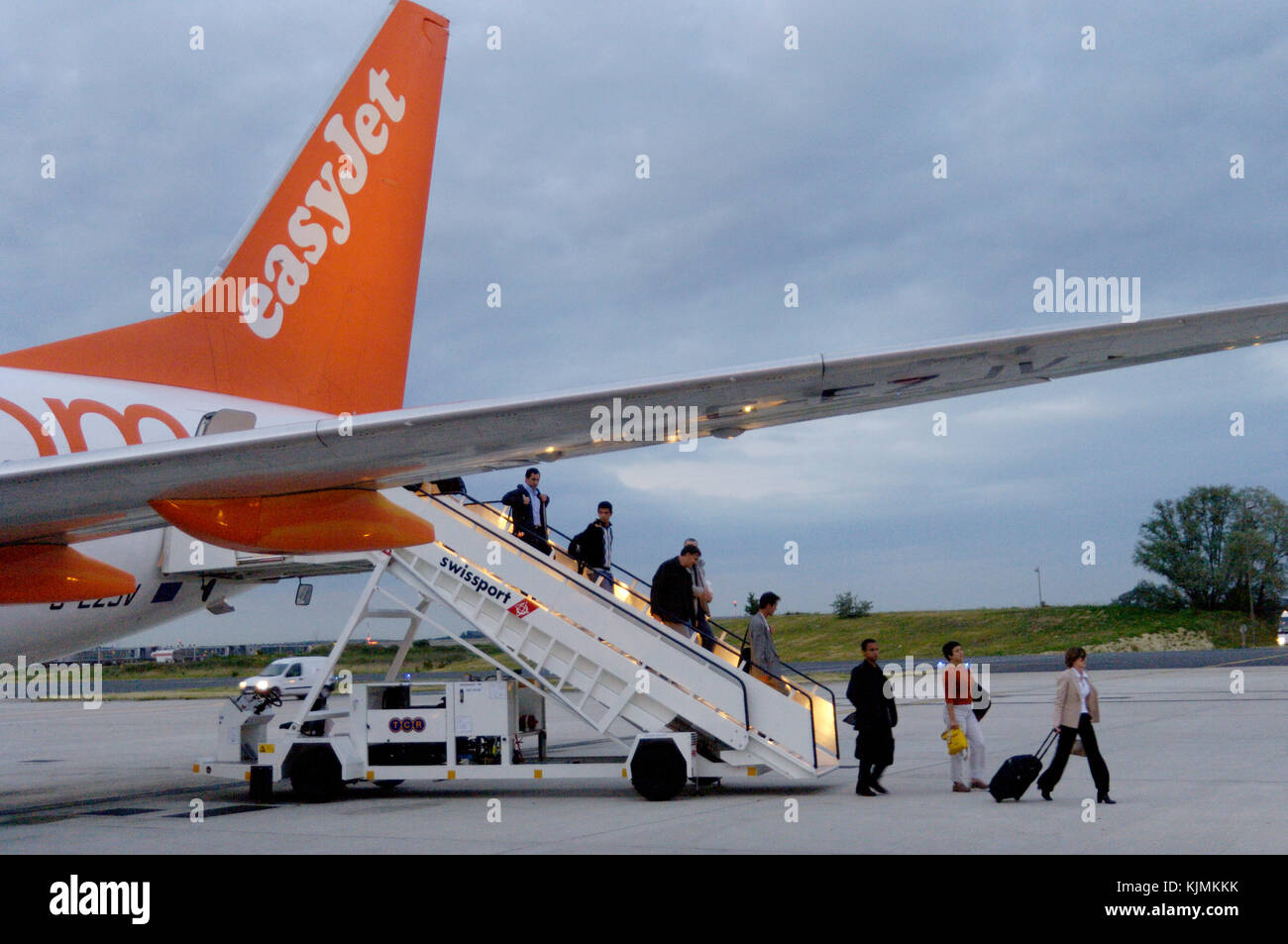 passengers disembarking a remote parked easyJet 737 via the rear Swissport airstairs at night and a woman with carry-on baggage Stock Photo