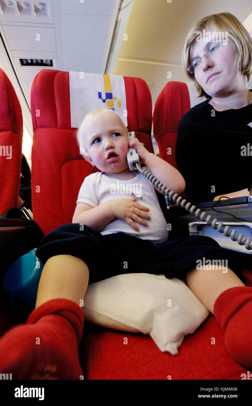 mother and 1.5 year old baby boy Henry with the video / audio control unit and satellite telephone on a long haul flight in the economy-class cabin LG Stock Photo