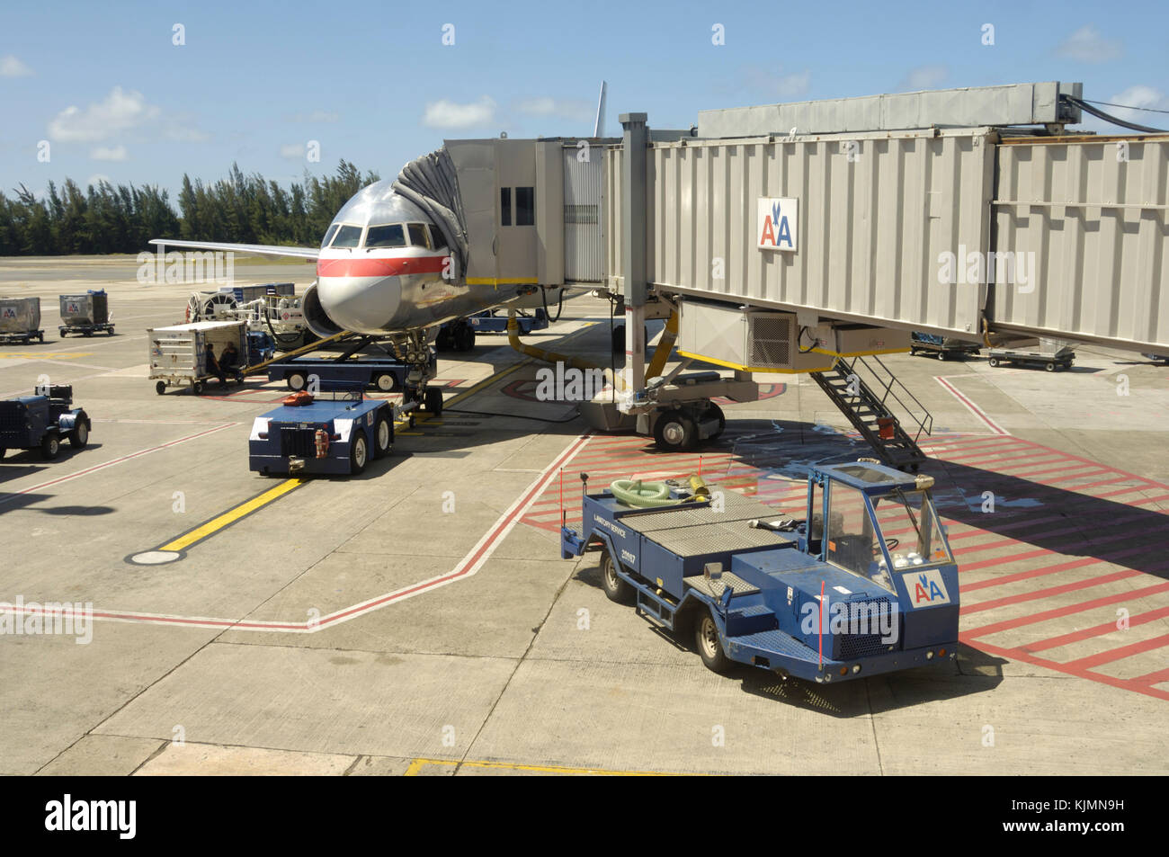 American Airlines Boeing 757-200 parked with tug, baggage-belt truck, trolleys and jetway attached Stock Photo
