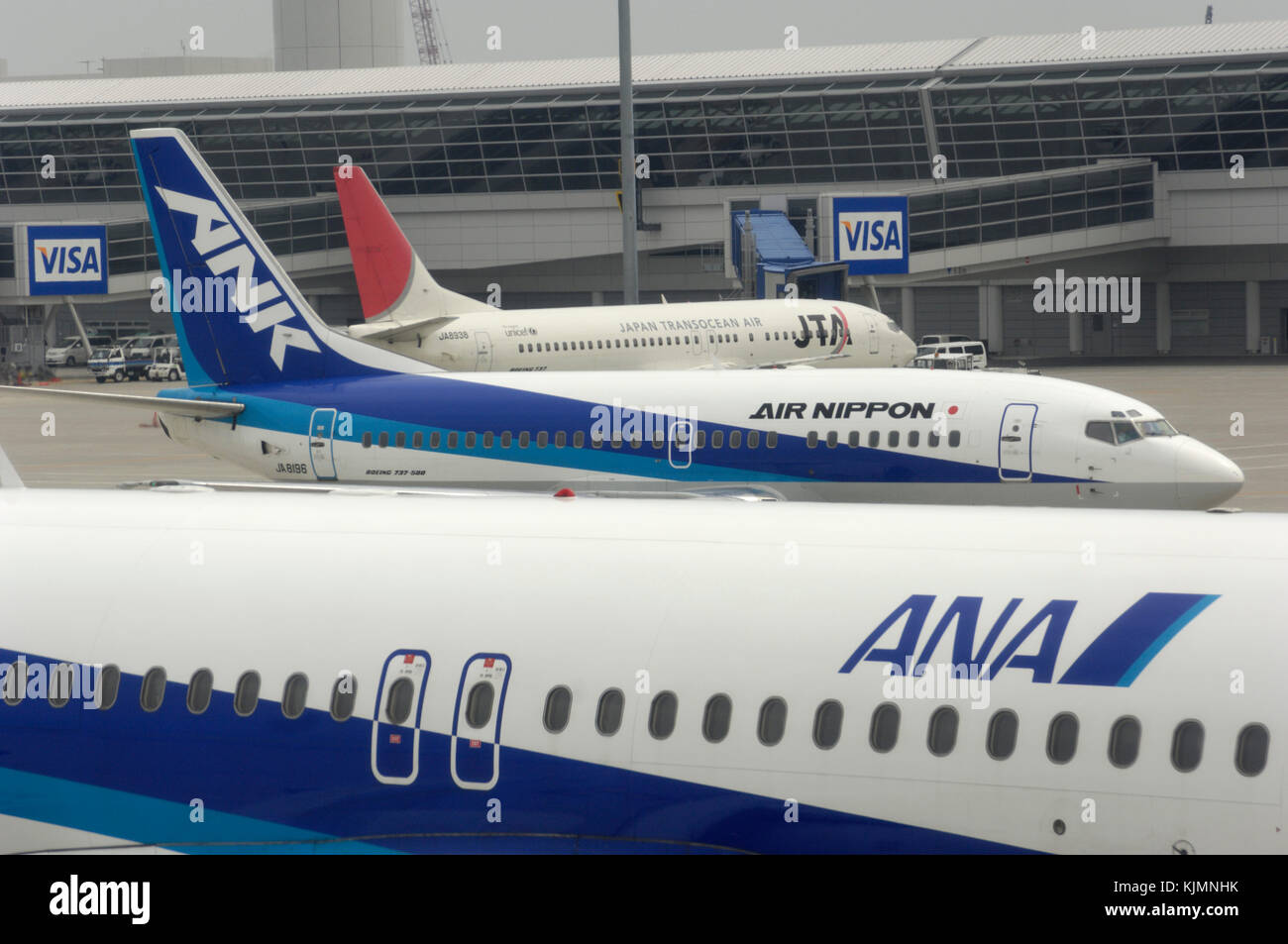 an ANA All Nippon Airways Airbus A320-200 with an ANK Boeing 737 taxiing and a JTA B737 parked at the terminal behind Stock Photo