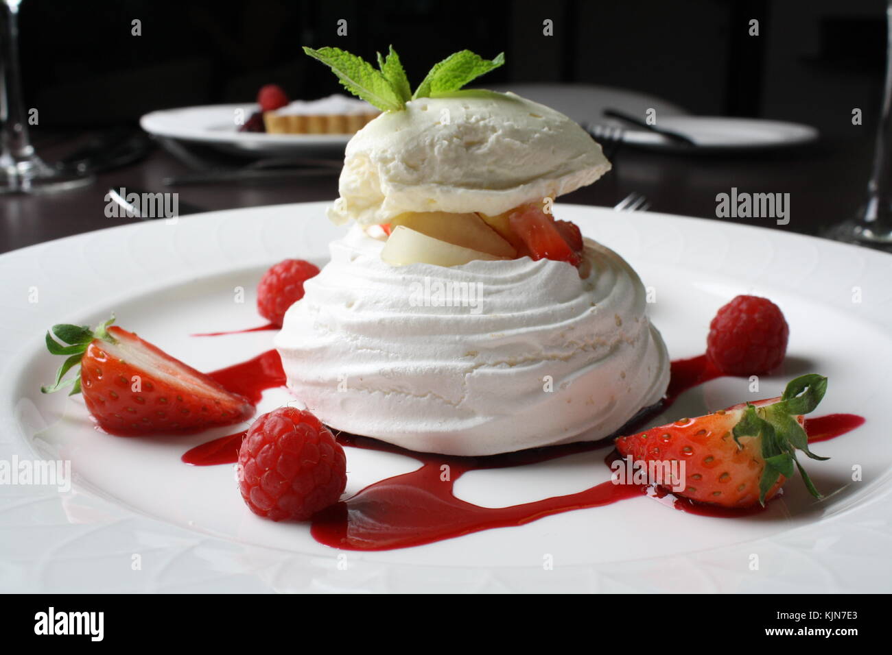 close up of strawberry meringue dessert with fruit sauce on plate in