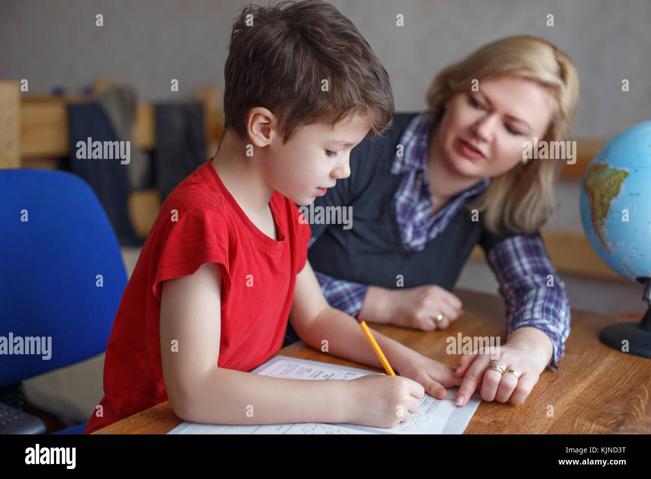 Mother helps son writing homework into exercise book, helpful hand, studying together at home on desk Stock Photo
