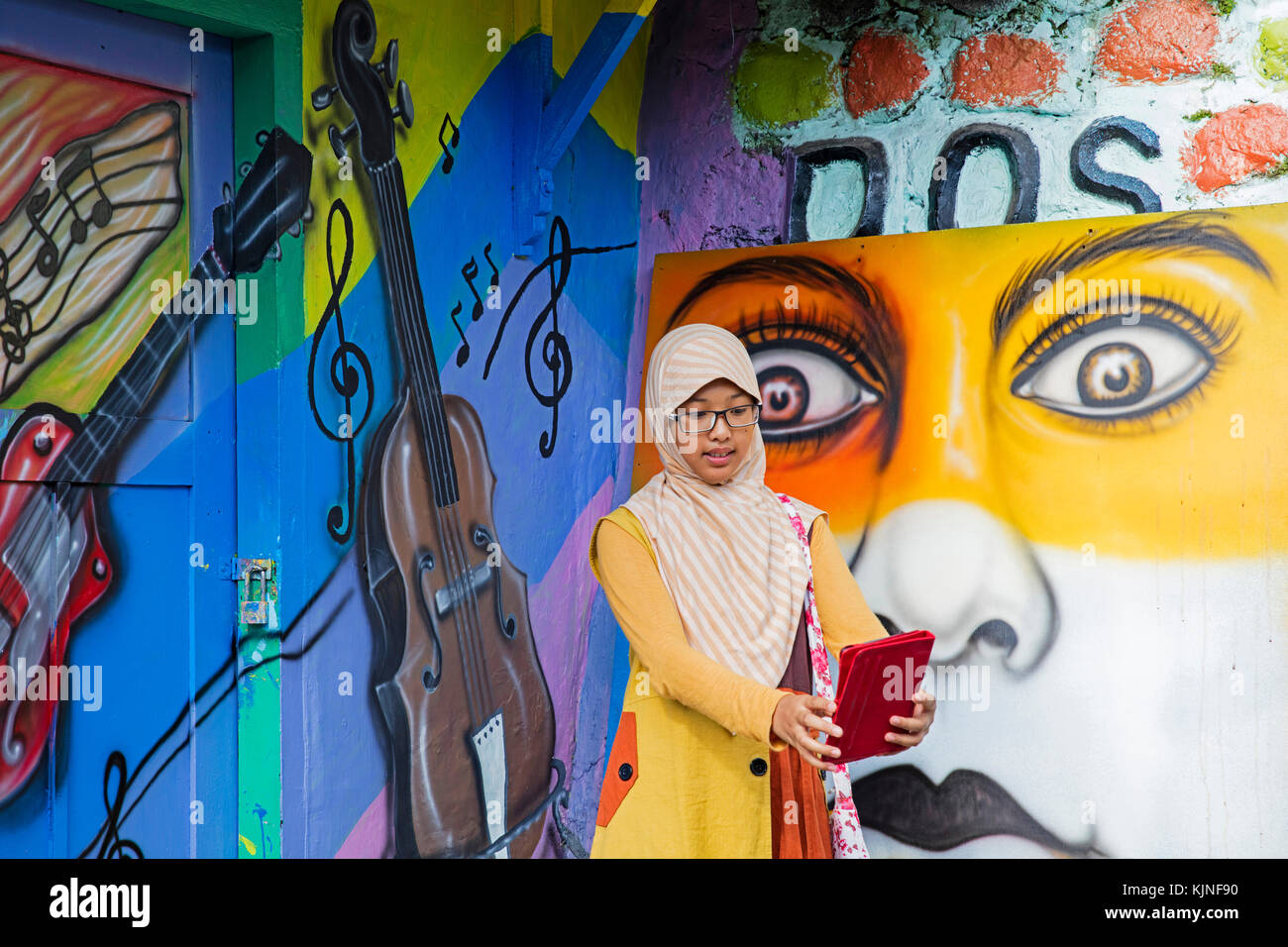 Young Indonesian girl taking selfie with tablet in Kampung Wisata Jodipan, artist suburb of the city Malang, Jawa Timur / East Java, Indonesia Stock Photo