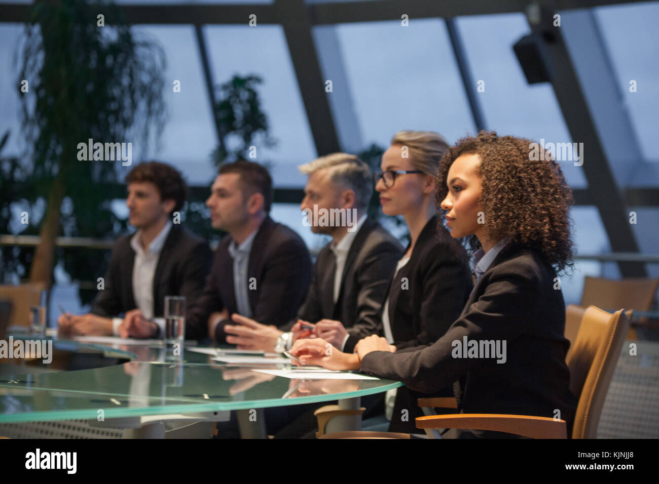 A group of business people sit at a table in a line and are discussing ...