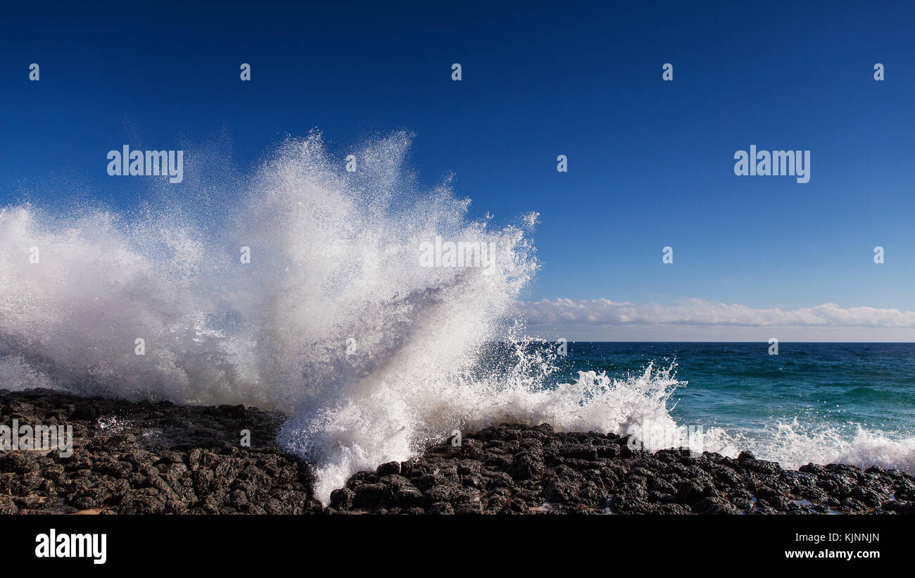 Wave smashes on rocky shore as tide surges in Stock Photo