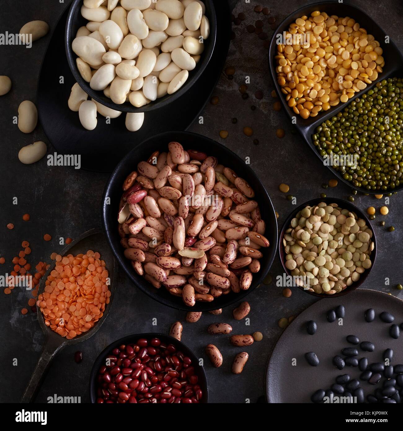 Pulses in bowls against dark background, overhead view. Stock Photo