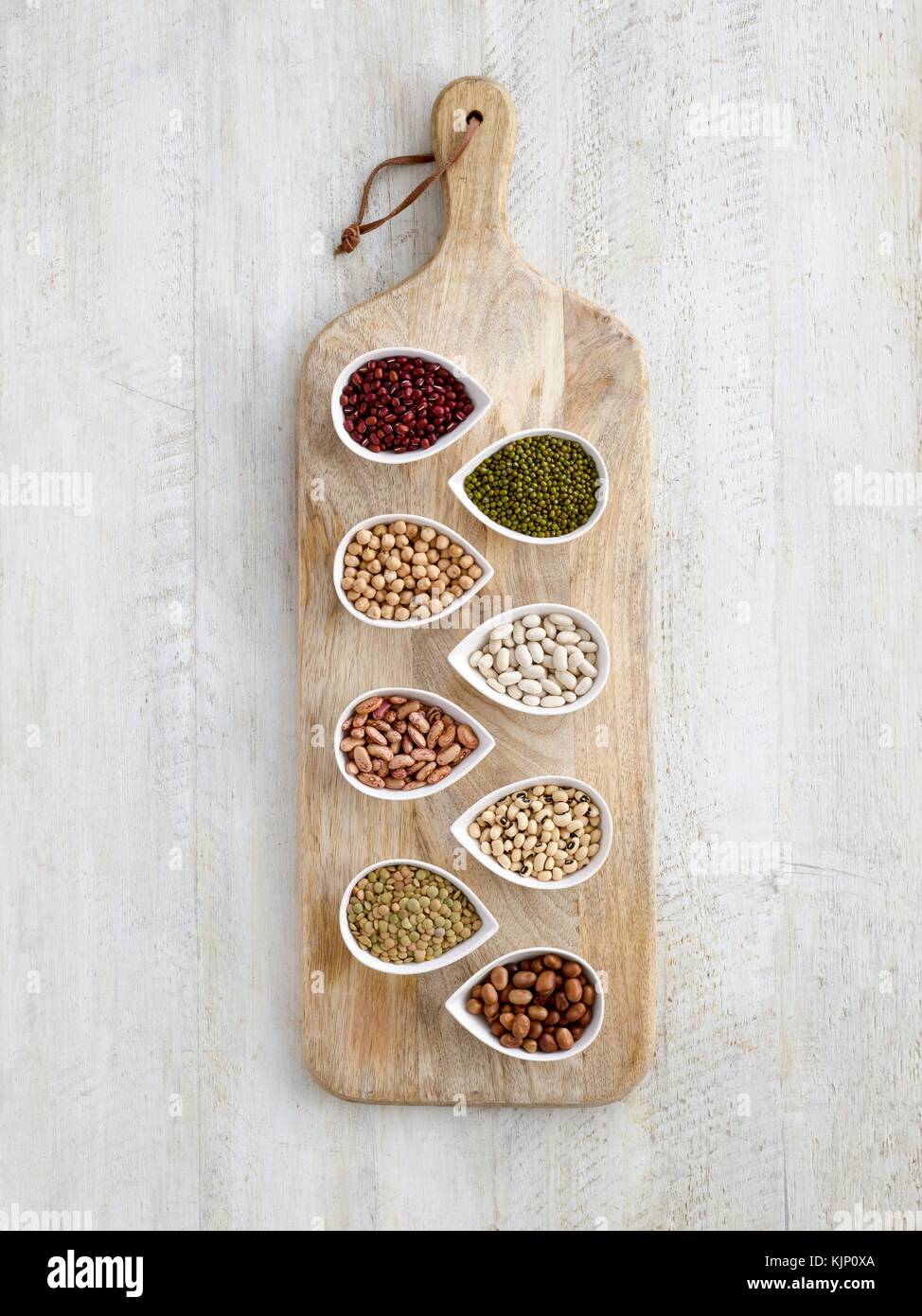 Pulses in tear shaped mini bowls on a chopping board, overhead view. Stock Photo