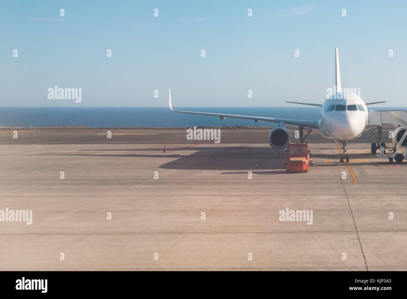 front of airplane standing on runway with ocean background Stock Photo