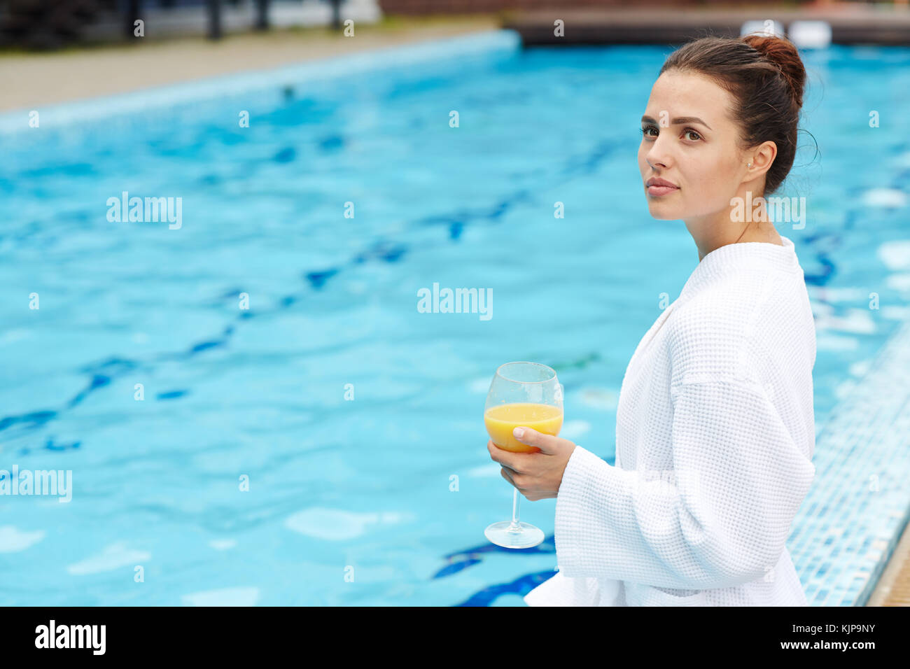 Young in white bathrobe having rest by swimmingpool with blue