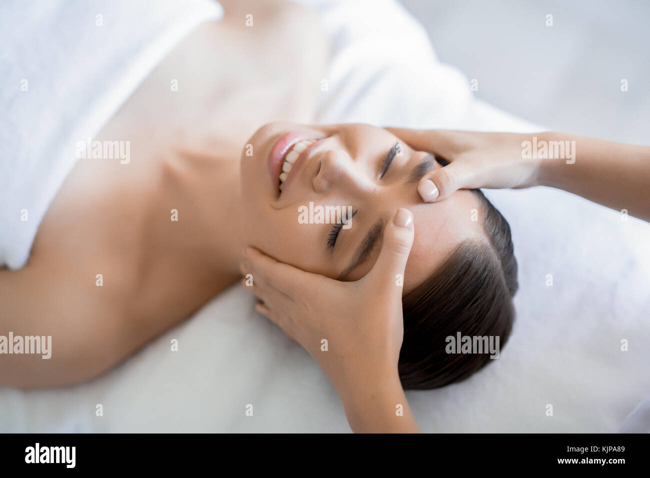 Masseuse keeping her hands on forehead of young client during massage of face Stock Photo