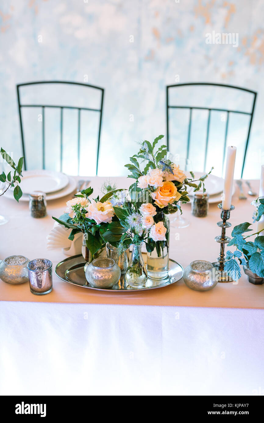 holiday, art, flora concept. still life composed of few small bunches of various flowers on the tray, lots of different candleholders and serveware arranged on the light pink tableware Stock Photo