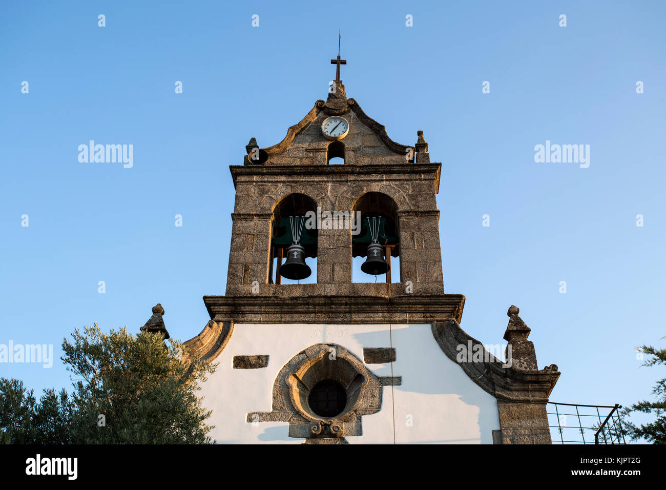 Parish church of Sao Romao with double bells, clock and cross on top of a truncated gable, in Bacal, Braganca, Portugal Stock Photo