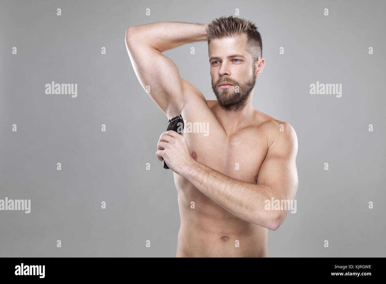 Handsome Young Bearded Man With A Trimmer Shaving Off Body Hair
