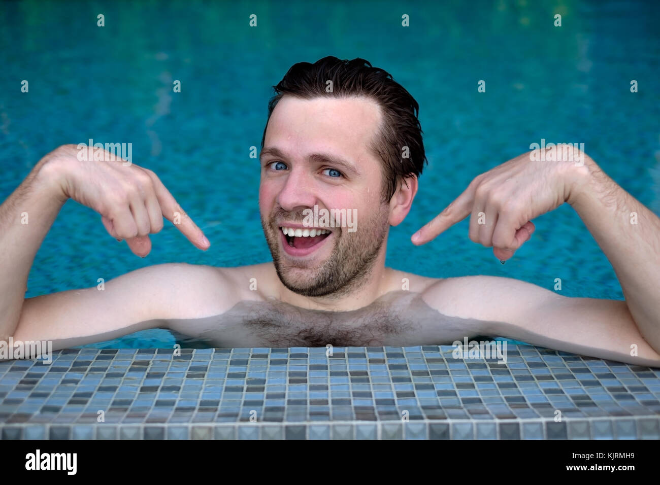 Proud caucasian young man looks forward showing with index fingers on himself. He is swimming in pool during vacation Stock Photo