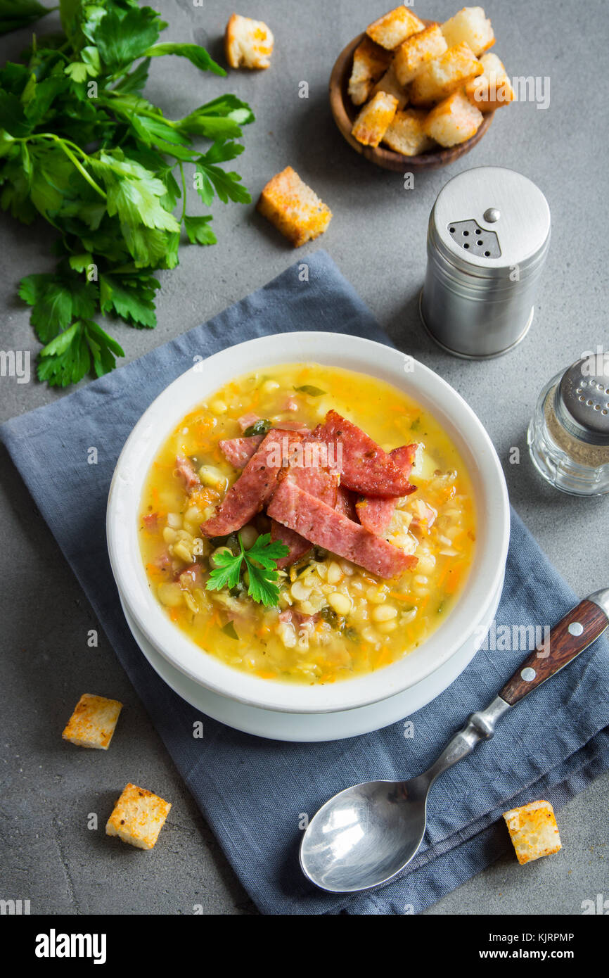 Split pea soup with smoked ham and croutons on grey background. Healthy