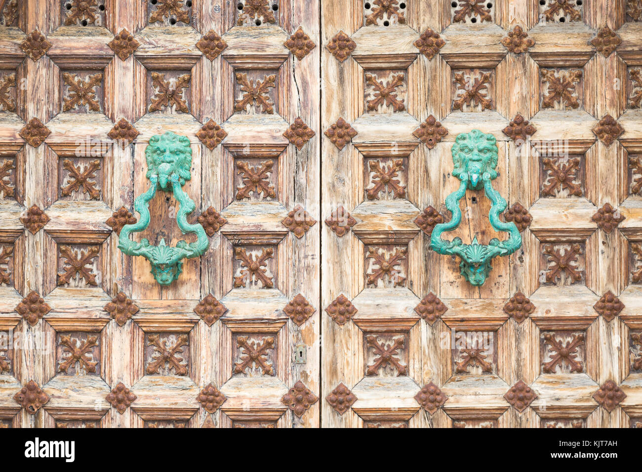 Closeup of ornate wooden medieval door with two turquoise lion head handles in Sitges, Spain Stock Photo