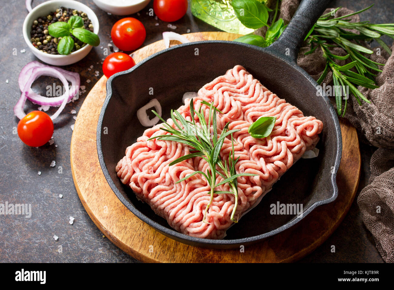 Raw minced beef on a cast iron frying pan, and a variety of spices, vegetables and herbs. Stock Photo