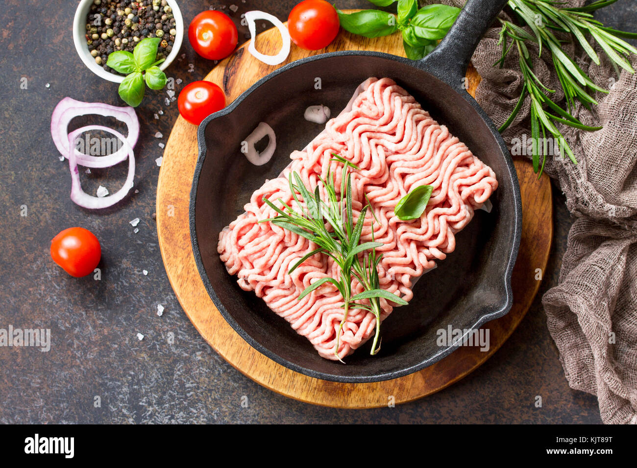 Raw minced beef on a cast iron frying pan, and a variety of spices, vegetables and herbs. Stock Photo