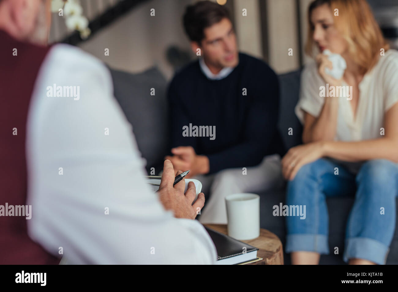 Psychologist consulting young couple in trouble. Psychotherapist taking down notes during counseling session. Stock Photo