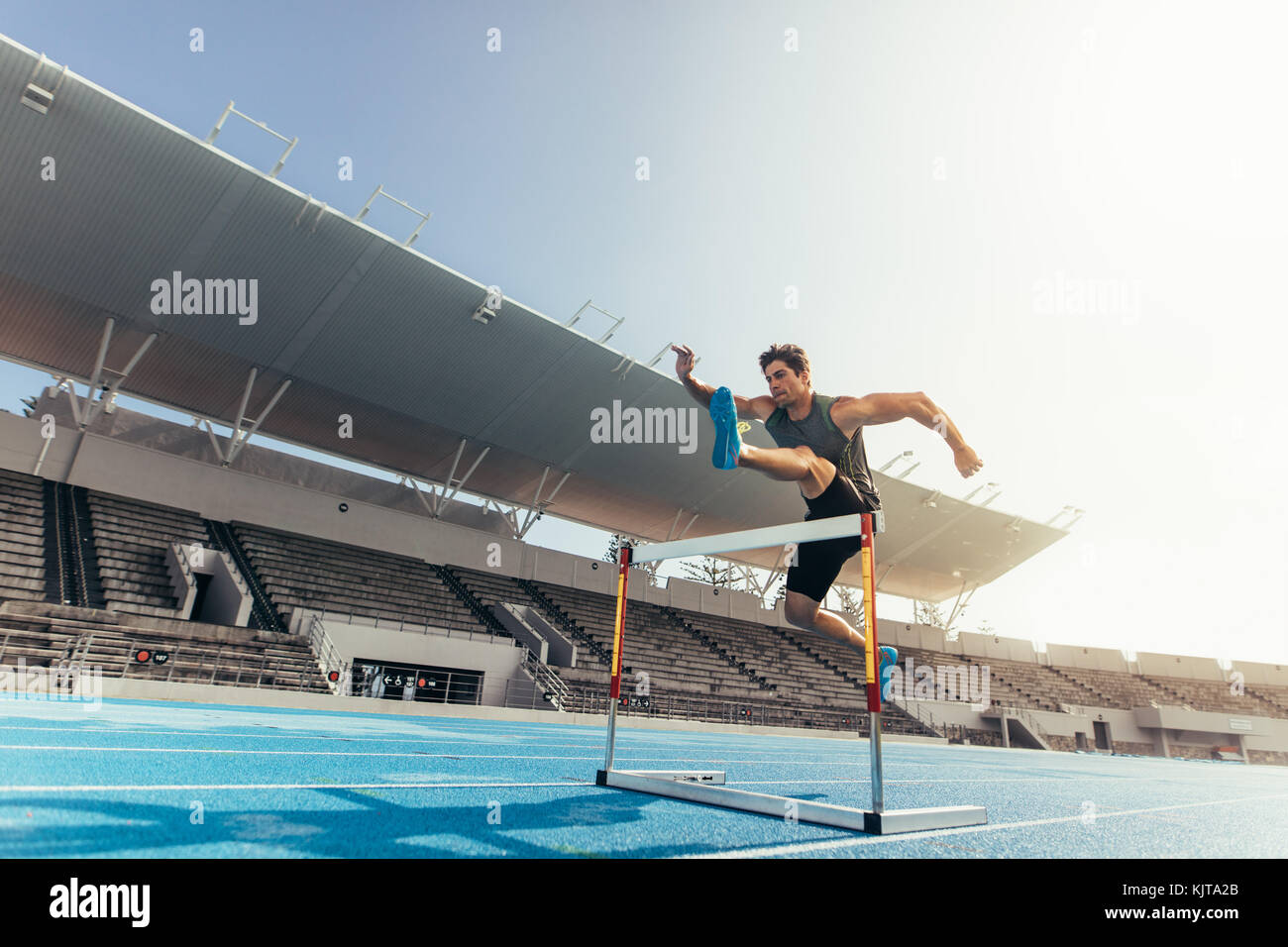 Runner jumping over an hurdle during track and field event. Athlete running a hurdle race in a