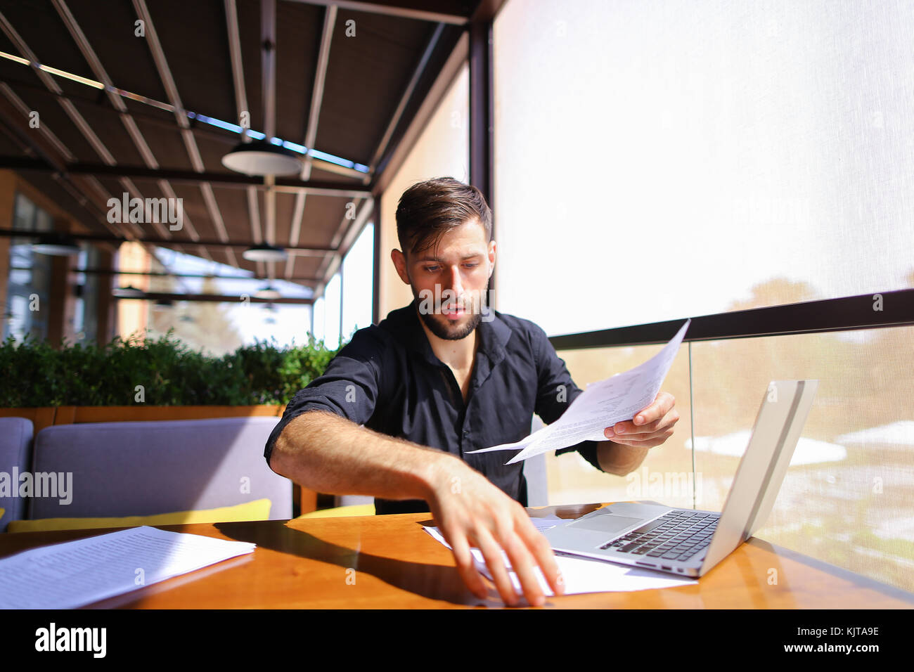 Office worker sorting papers on table near laptop. Stock Photo