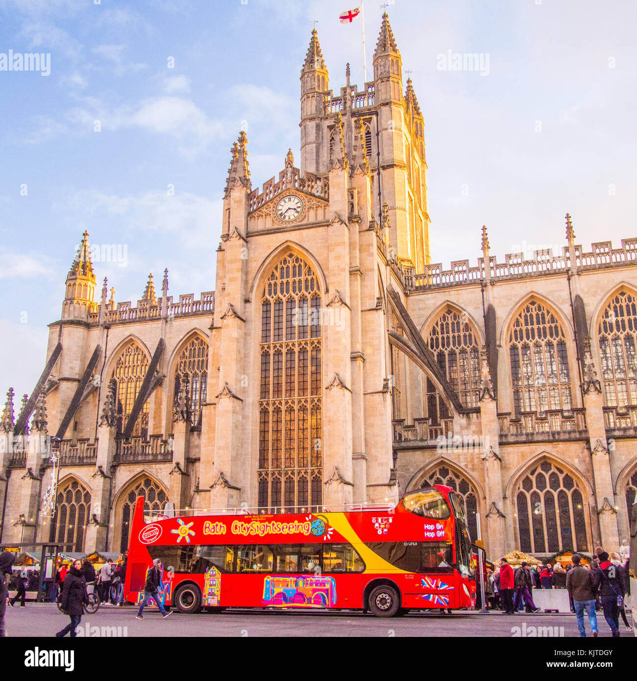 Sightseeing bus in front of Bath Abbey, a Gothic Church, Somerset, England.Christmas market stalls are on either side of the bus. Stock Photo