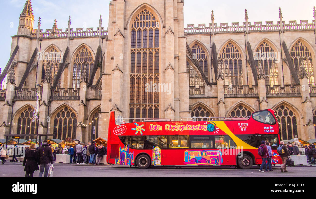 Sightseeing bus in front of Bath Abbey, a Gothic Church, Somerset, England.Christmas market stalls are on either side of the bus. Stock Photo