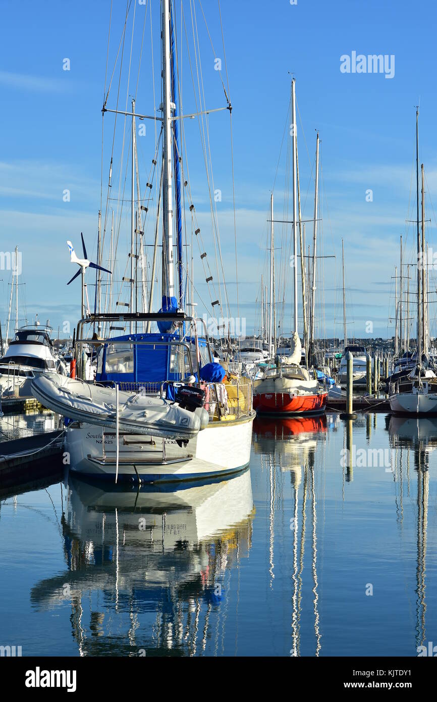 Sail ships with tall masts berthed in marina and reflecting on calm water surface. Stock Photo