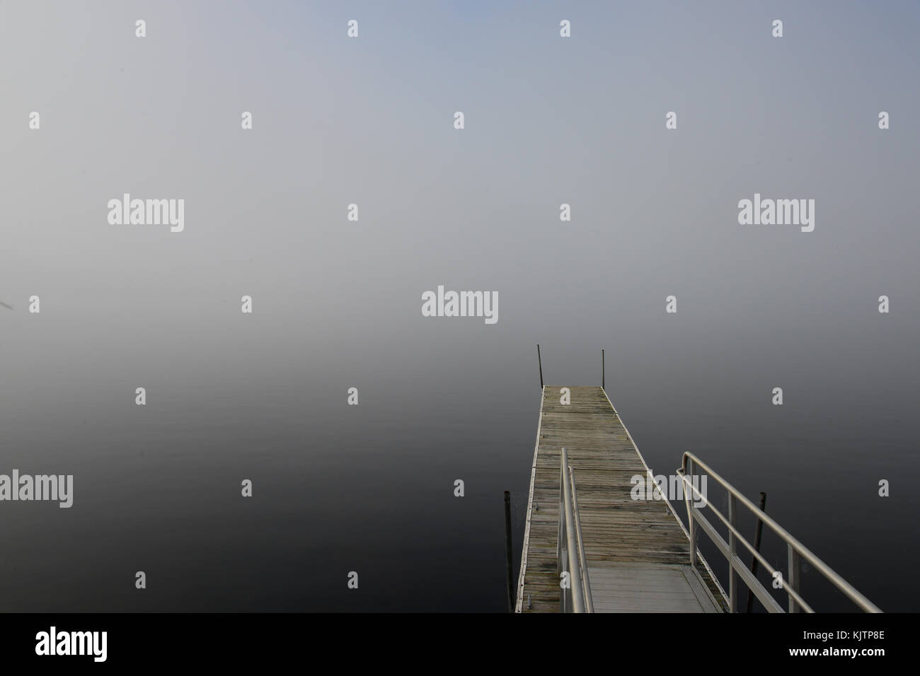 Dock on a foggy early morning lake scene with a hint of blue sky above the fog. Stock Photo