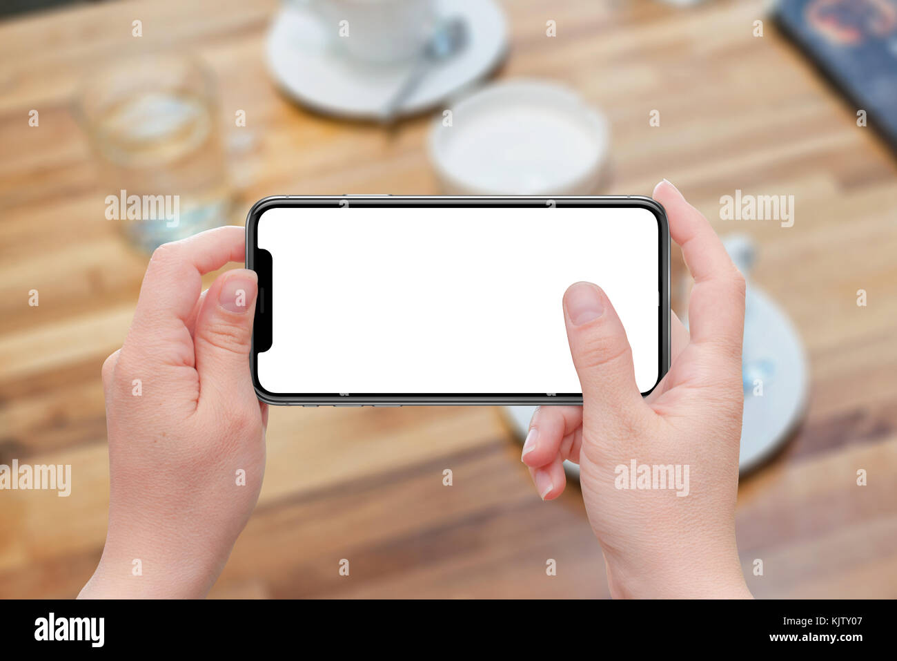 Woman holding modern smart phone in horizontal position. Isolated white screen for mockup design promotion. Coffee table in background. Stock Photo