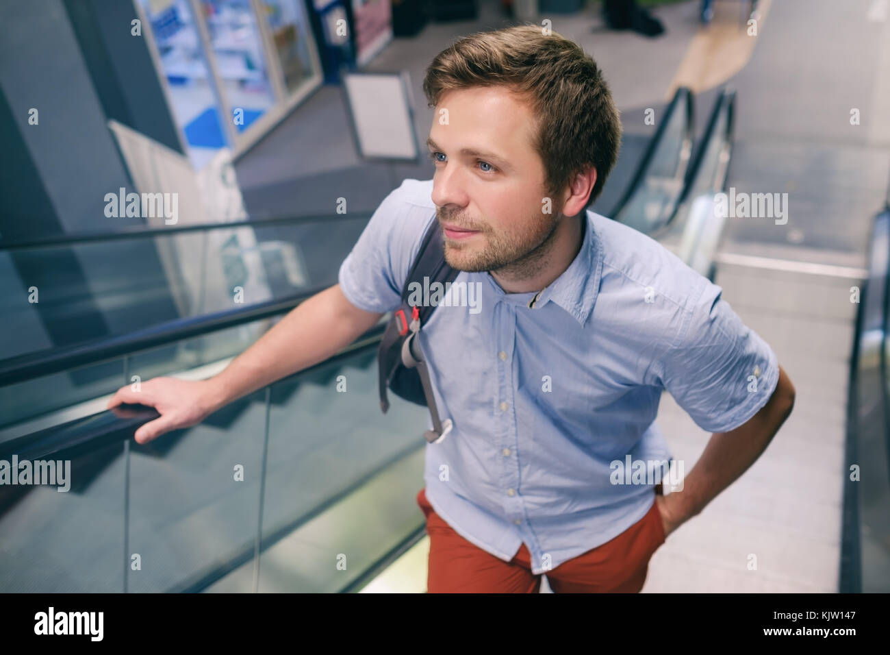 Young caucasian man moving up on an escalator at the airport. Stock Photo