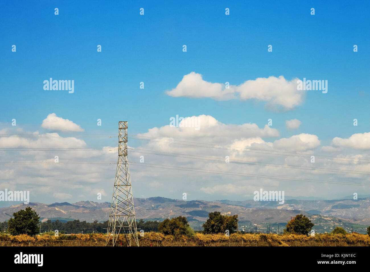 Electric power tower framed by a beautiful rural landscape with blue sky and white clouds. Stock Photo