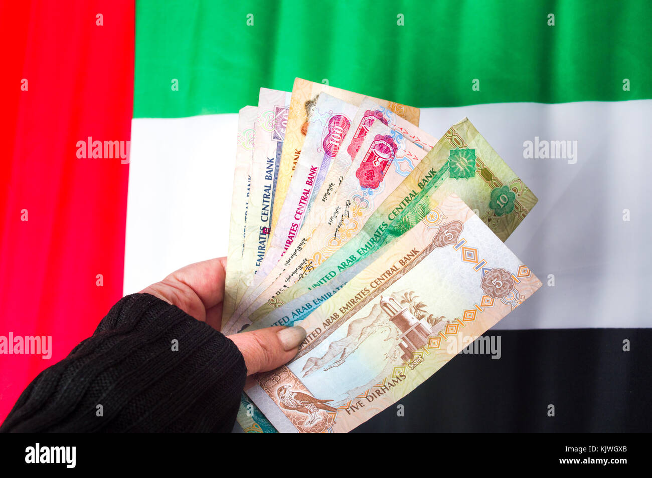 Hand holding United Arab Emirates dirhams on top of flag Stock Photo