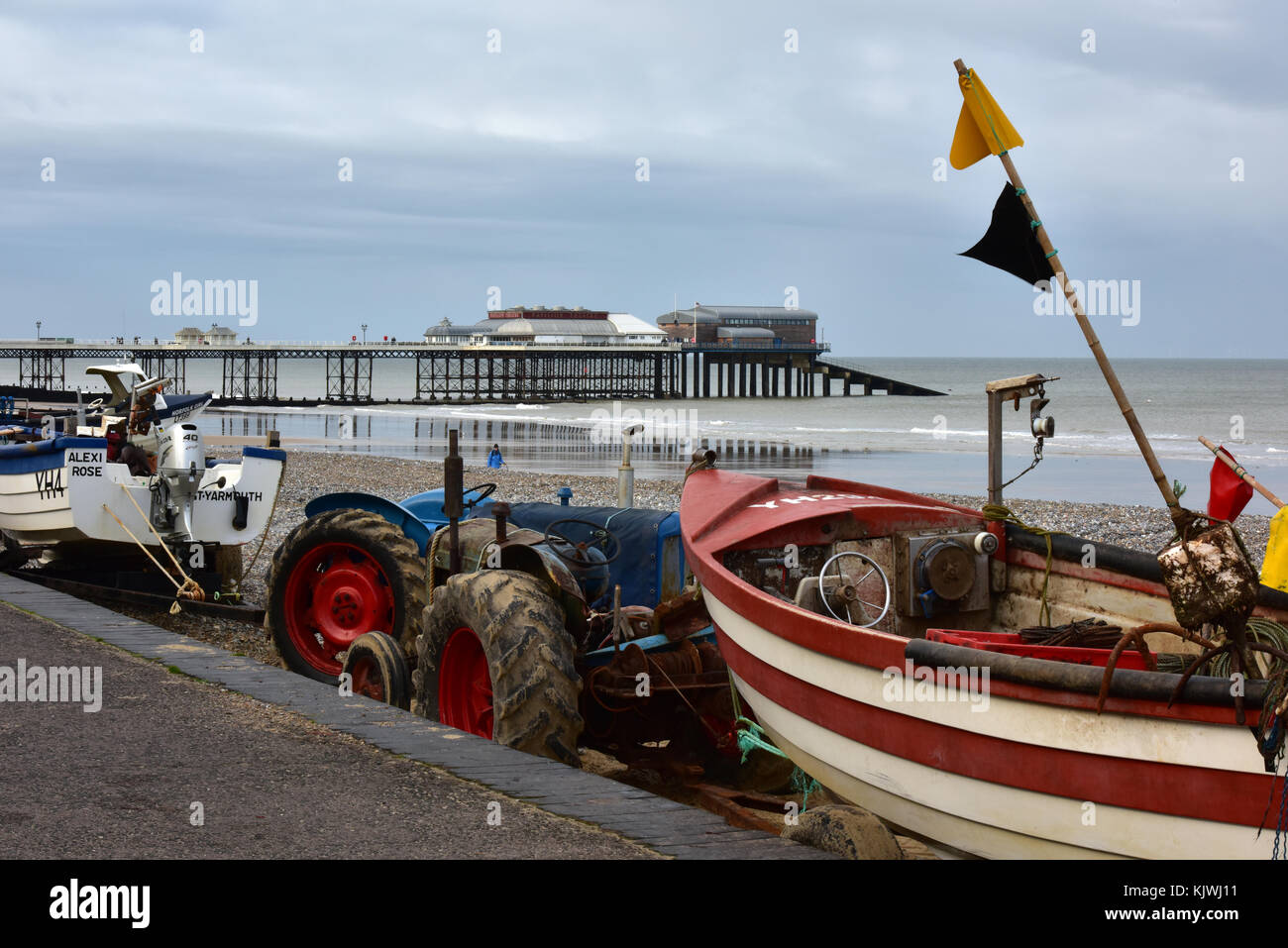 Traditional crab fishing boats and launching tractors in front of the Victorian pier at Cromer