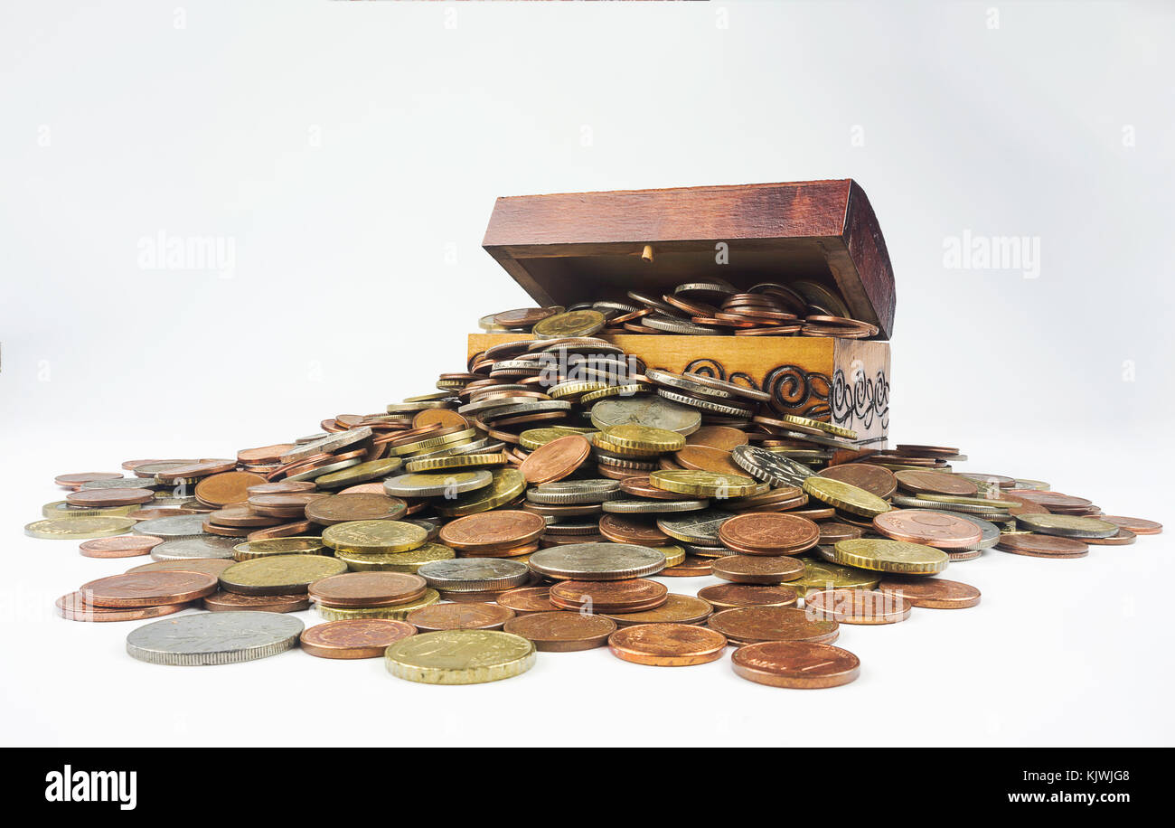 A small wooden treasure chest which is bursting with coins on a white background. Isolated composition which is related to the economic and financial  Stock Photo