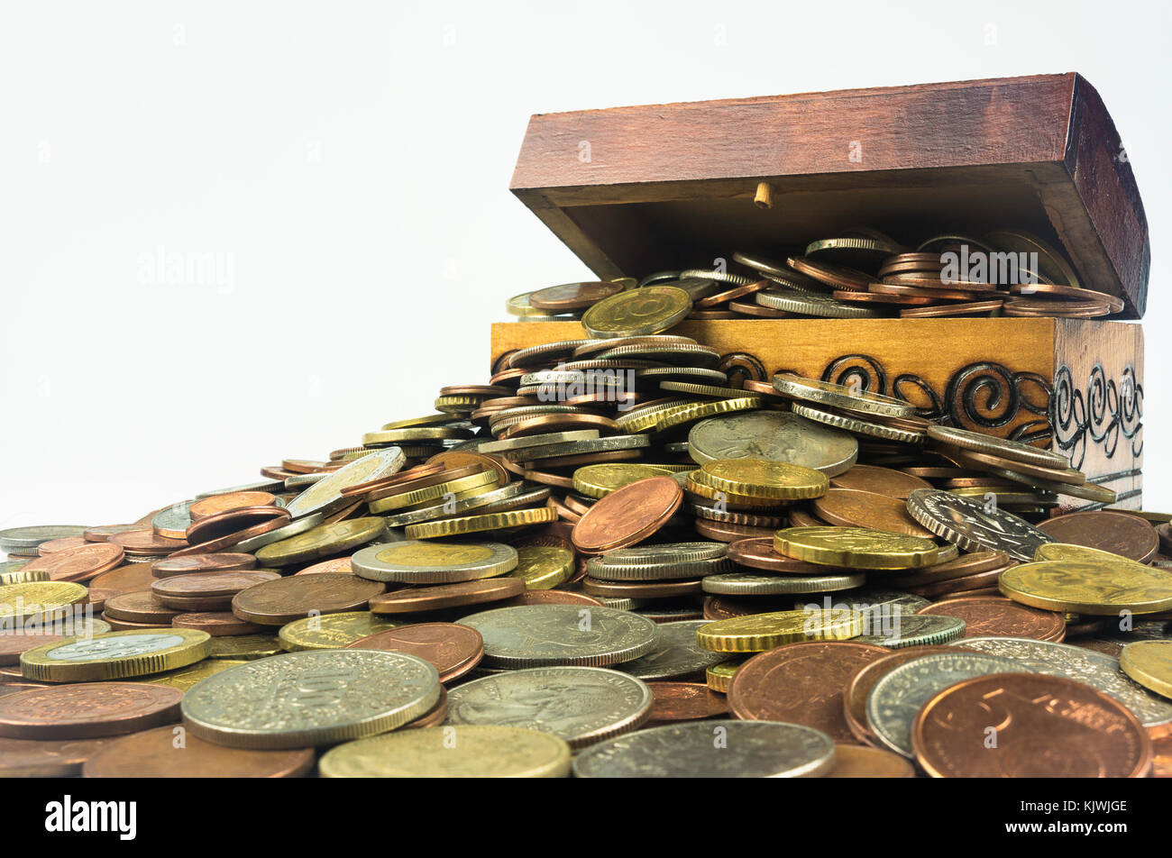 A small wooden treasure chest which is bursting with coins on a white background. Isolated composition which is related to the economic and financial  Stock Photo