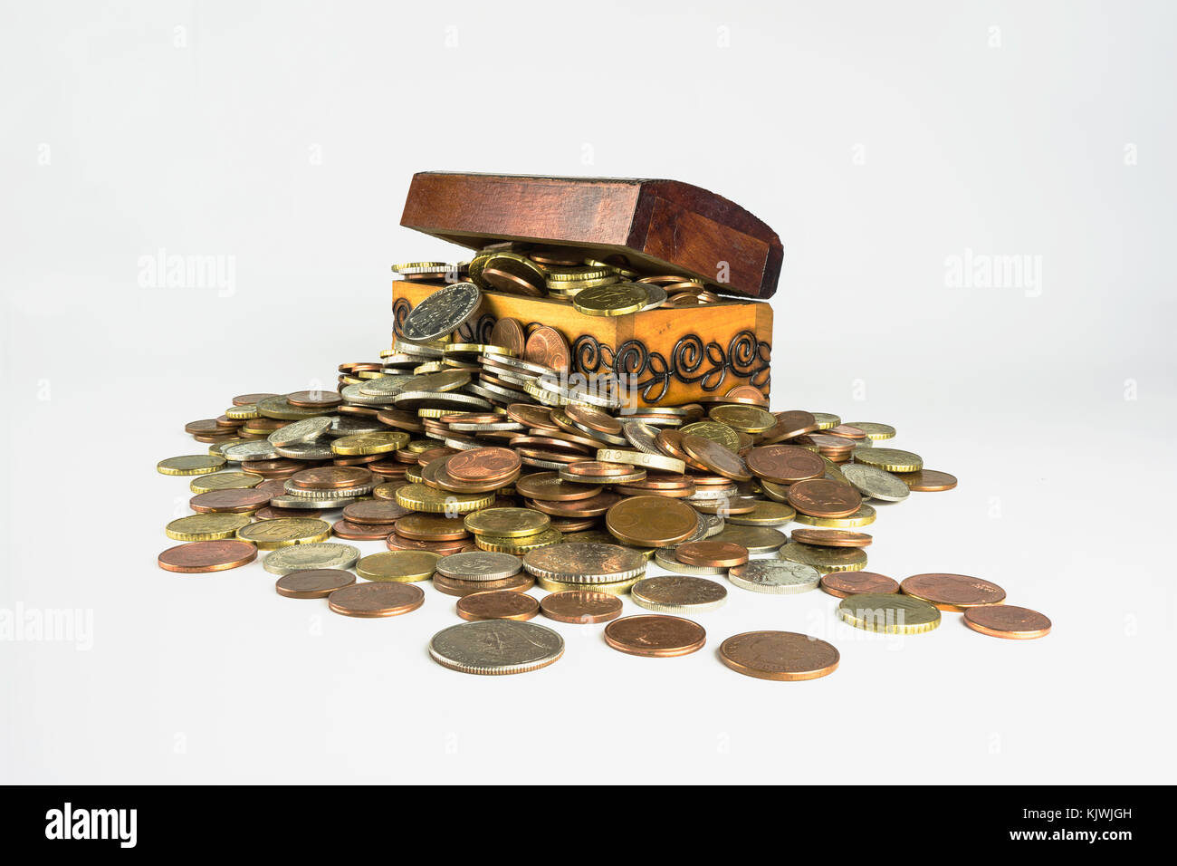 A small wooden treasure chest which is bursting with coins on a white background. Isolated composition which is related to the economic sphere Stock Photo