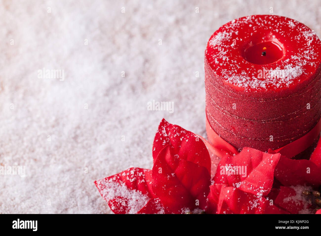 Christmas decoration, poinsettia and red decorative candle sprinkled with snowflakes. Stock Photo